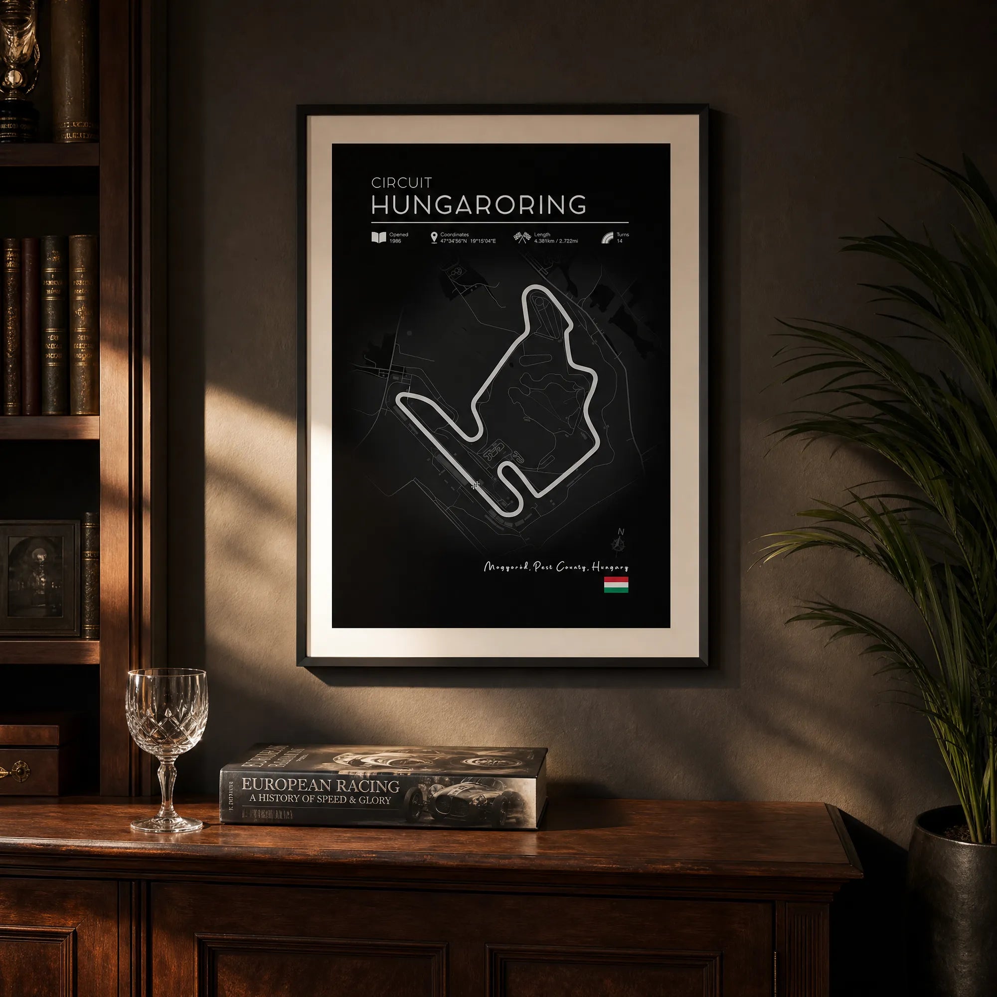 Race track art black edition Hungaroring poster above timber sideboard with wine glass and European racing book
