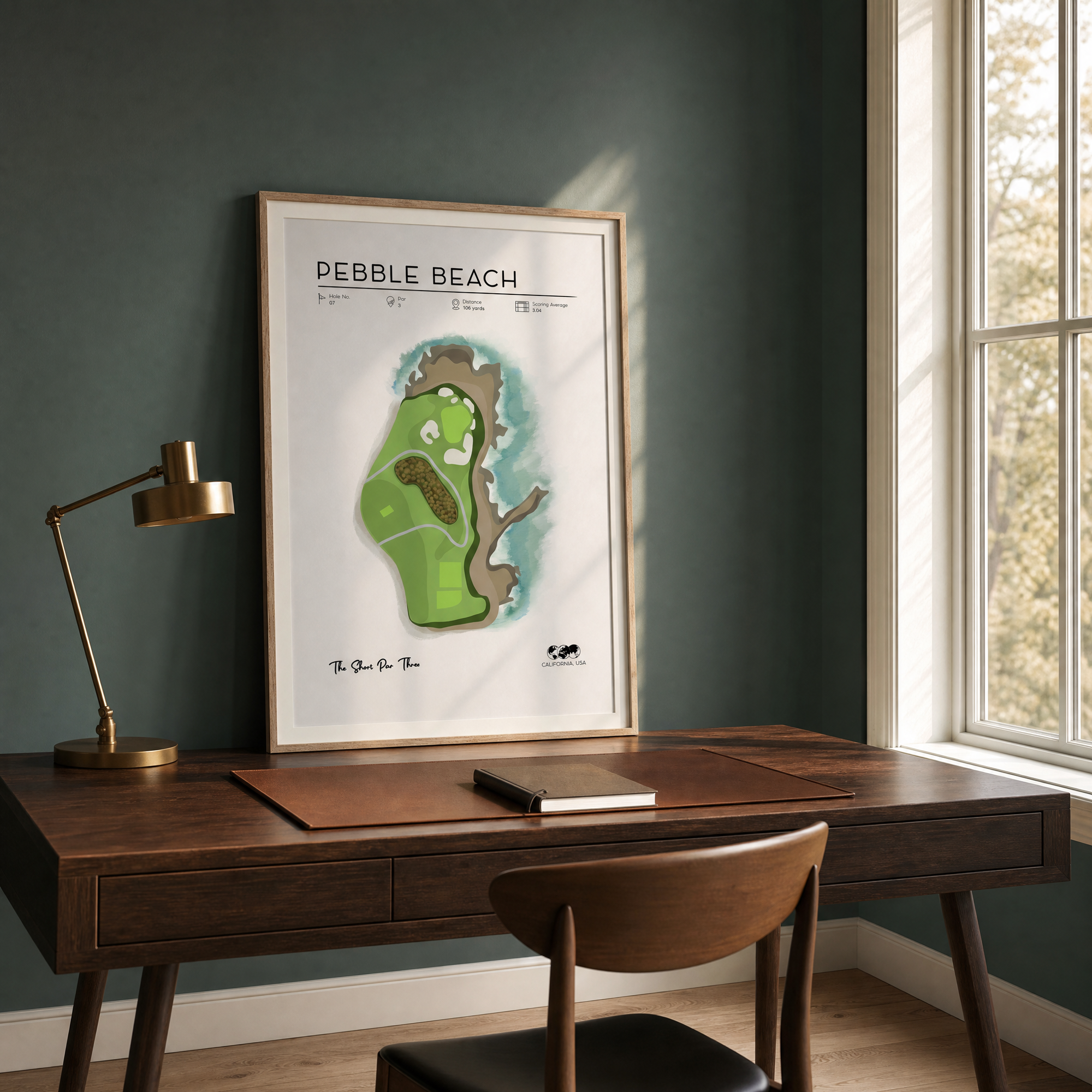Pebble Beach golf print in a light oak frame above a dark oak home office desk, teal-grey wall, natural morning light